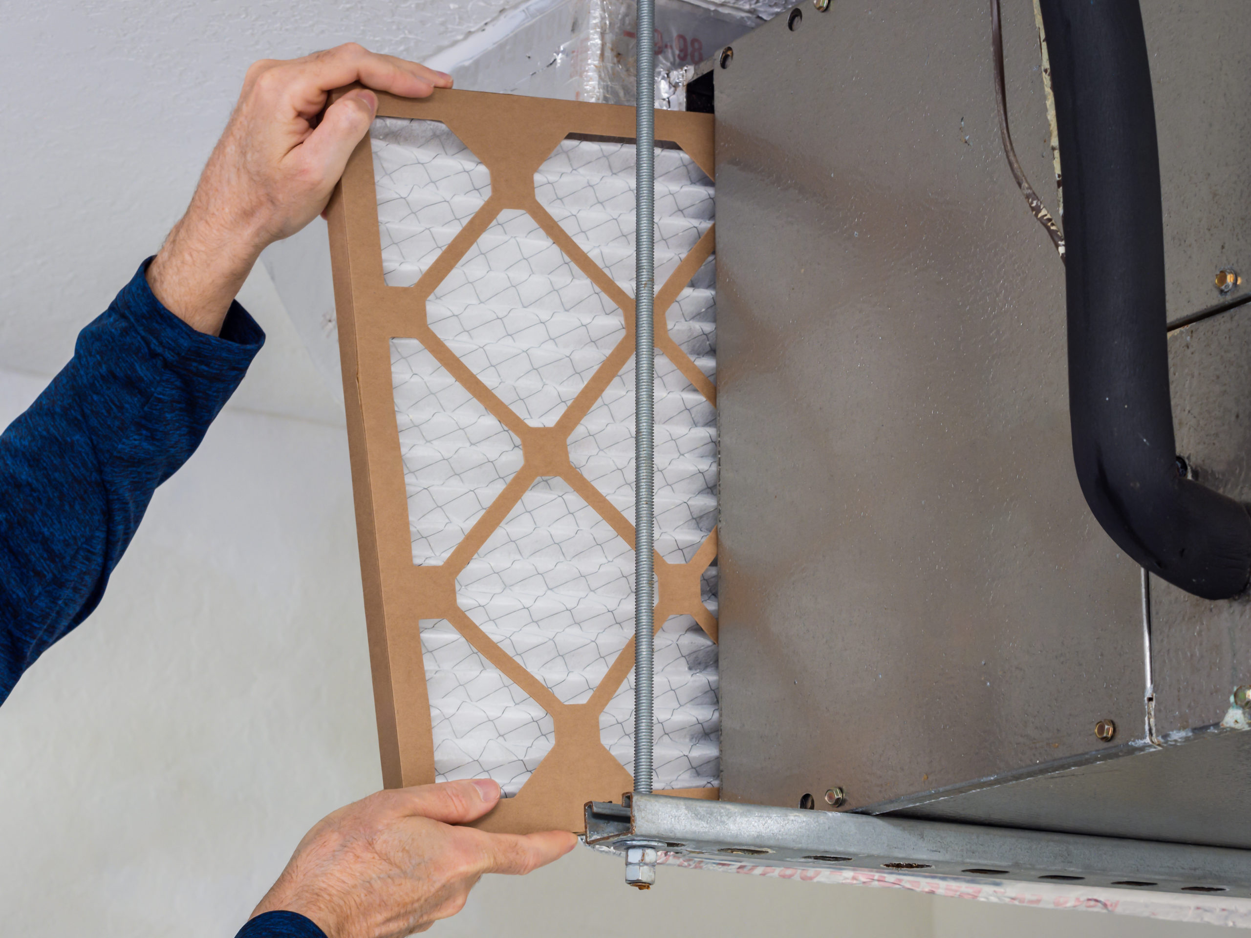 An HVAC technician replacing a gas furnace air filter.