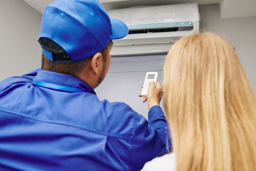 An HVAC technician and woman using a remote to switch on a ductless mini split unit.