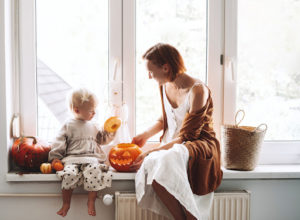 A woman and child sitting on a bench near a window. They are looking at a pumpkin.