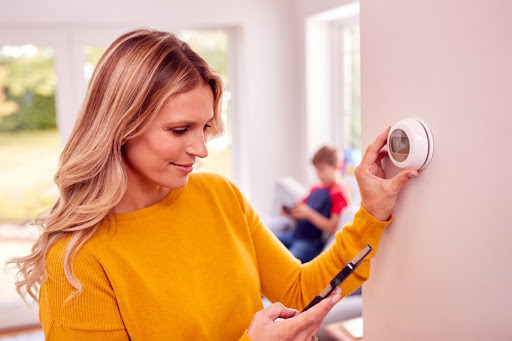 A woman adjusting a smart thermostat from her phone.