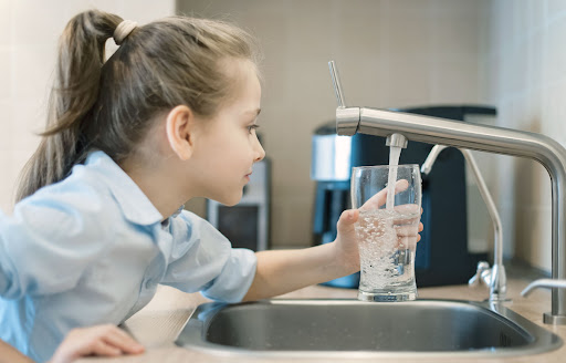 A girl filling a glass of water at a kitchen sink.
