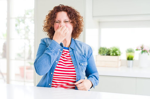 A woman holding her nose due to a bad smell.