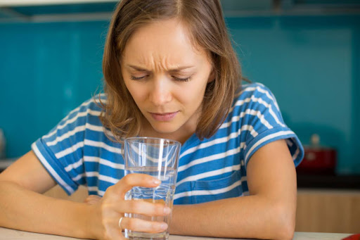 A woman with a puzzled expression looking at a glass of water.