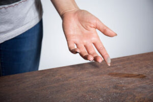 A hand touching the dust on a wood surface.