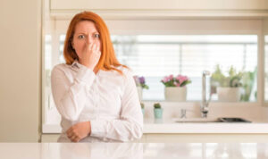 A woman holding her nose due to a bad smell in the kitchen.