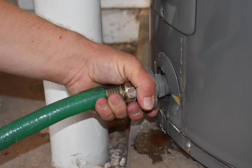 A close-up of a hand connecting a hose to a water heater drain valve.