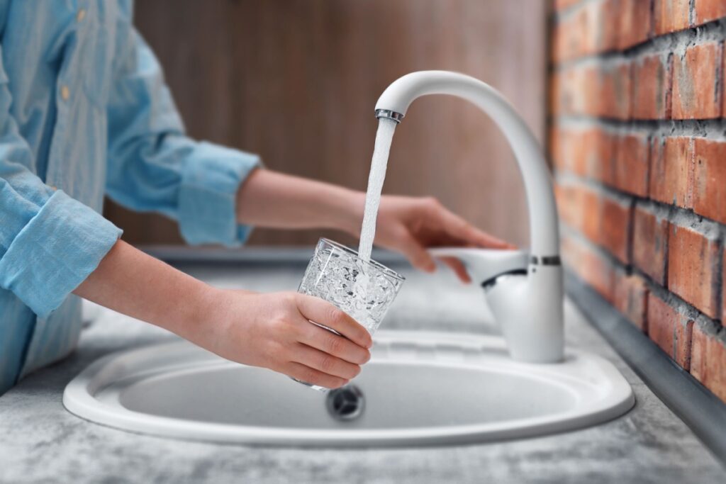 A woman filling a glass with water from a tap.