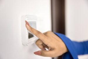 A close-up of a woman's hand adjusting a thermostat.