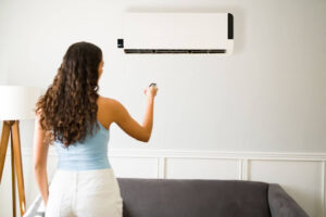 A woman using a remote to control an indoor ductless AC unit on a wall.