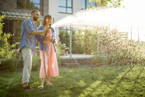 A couple using an garden hose to water a lawn.
