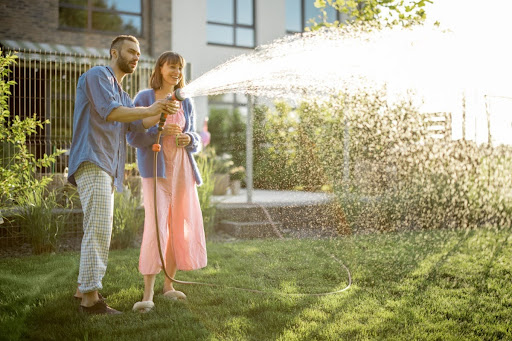 A couple using an garden hose to water a lawn.