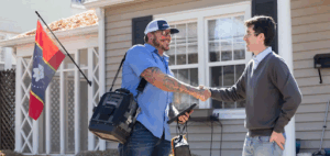 An HVAC technician shaking hands with a homeowner in front of a house.