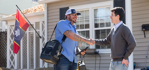 An HVAC technician shaking hands with a homeowner in front of a house.