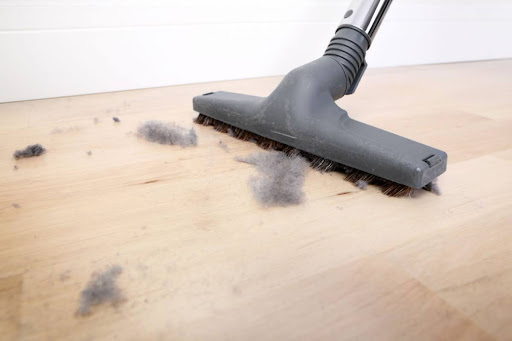 A vacuum being used to clean up dust on a wood floor.